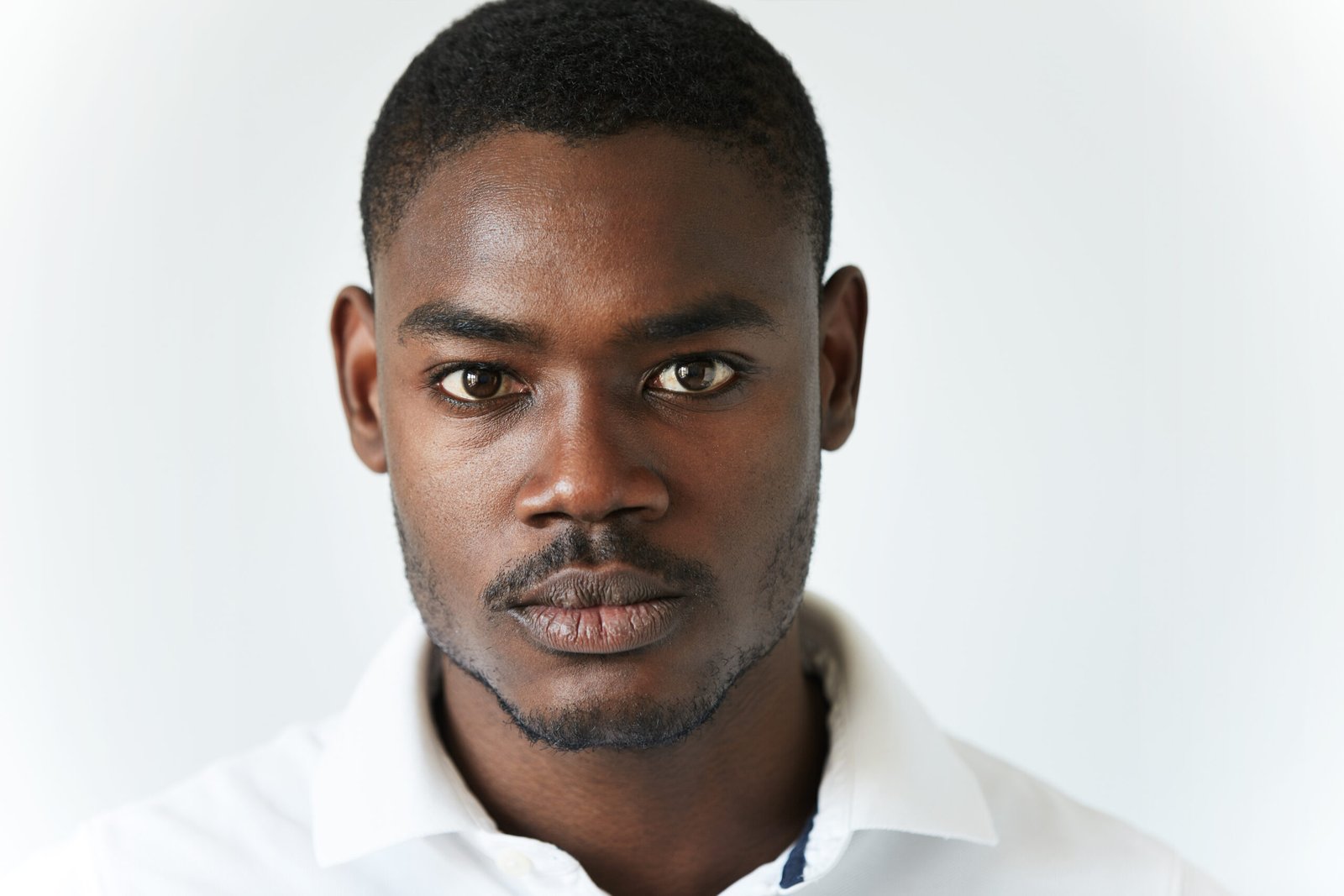 highly detailed close up portrait of handsome young african american man wearing stylish polo shirt, looking at the camera with serious thoughtful expression. human face expression and emotions